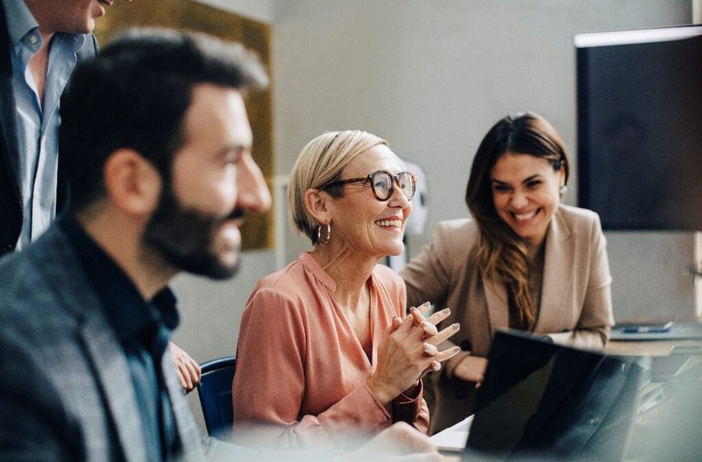 A group of happy employees collaborating in an office, representing how health insurance for company employees improves productivity and morale.