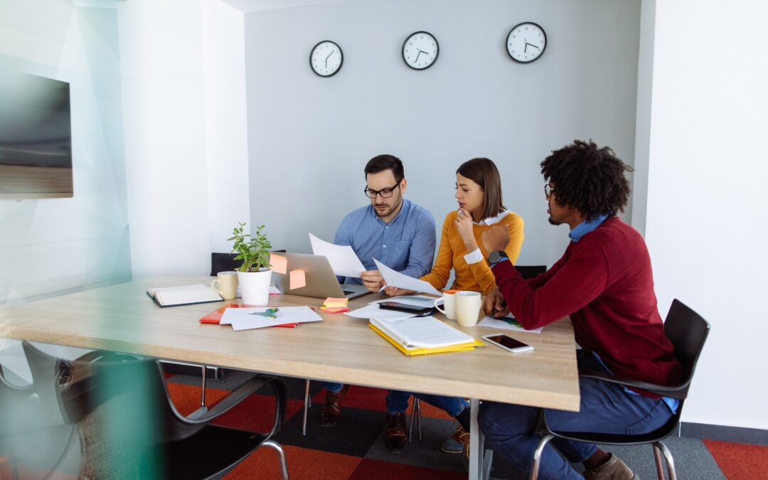 Three colleagues sitting at a conference table reviewing documents and discussing work in a modern office setting | Association health plan